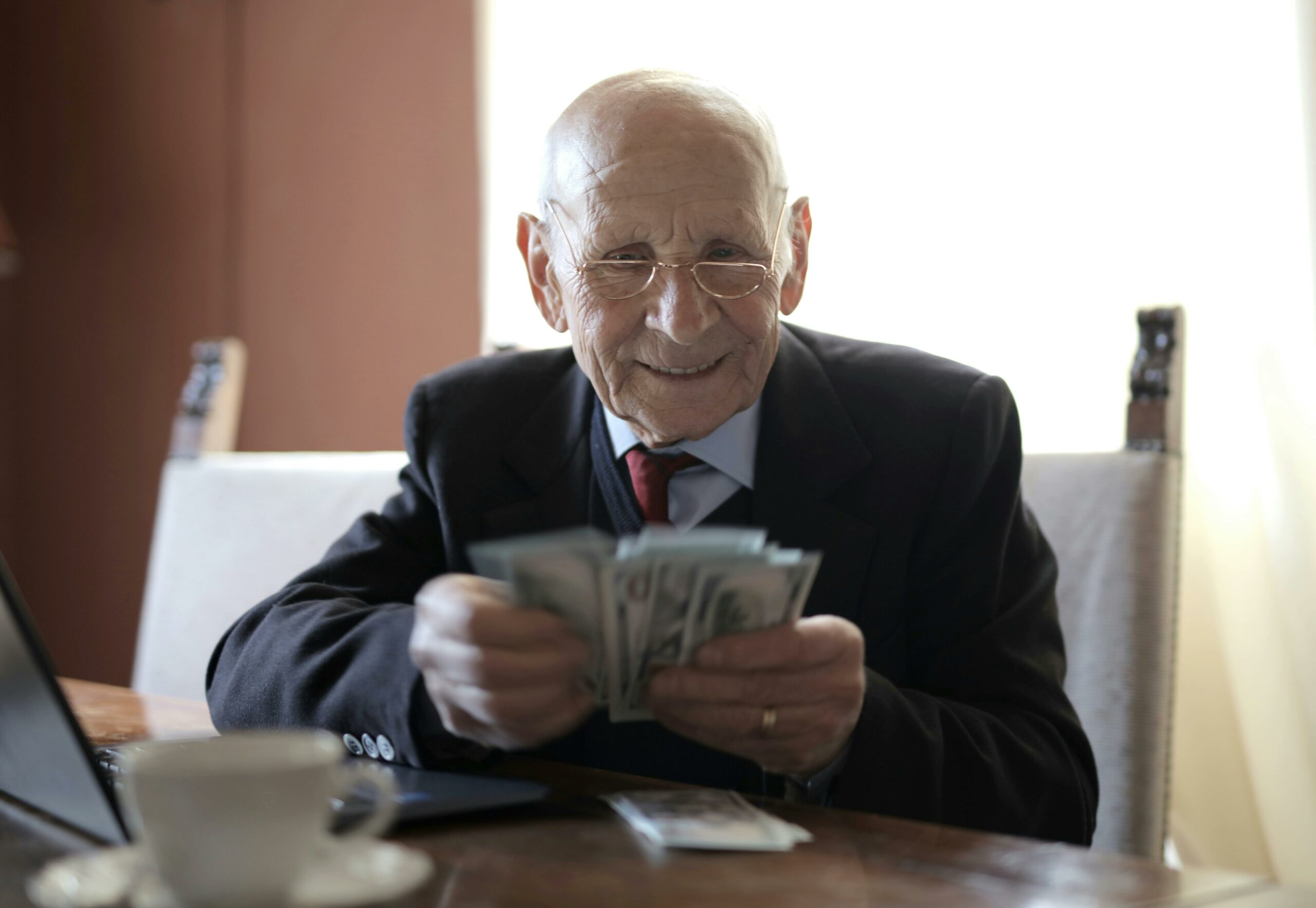 Glücklicher älterer Geschäftsmann, Der Geld Zählt, Während Er Am Tisch Mit Laptop Sitzt